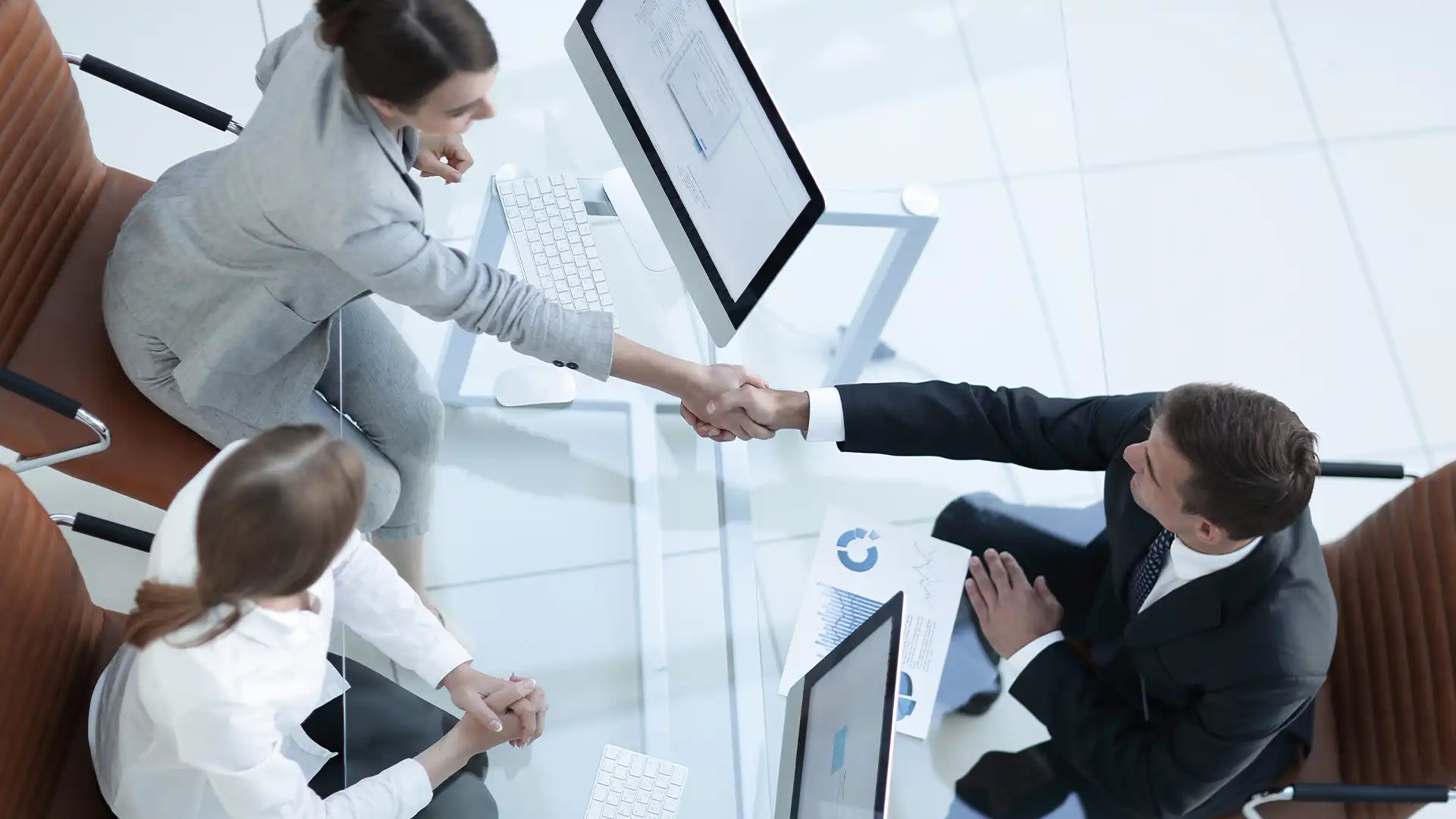 Two business professionals shake hands over a workstation, symbolizing a successful partnership in technology management. This image illustrates Prudent’s commitment to transforming your technology investments into strategic business assets through comprehensive assessments and adaptive innovations