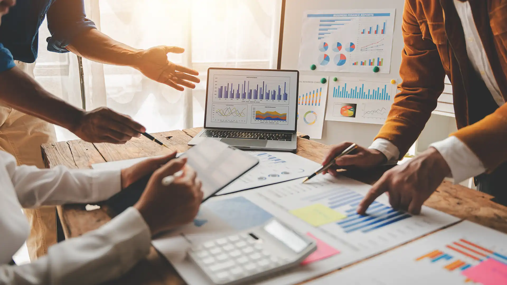 Business professionals discuss financial strategies with a laptop displaying detailed graphs and charts, symbolizing Prudent's expertise in invoice management and financial optimization