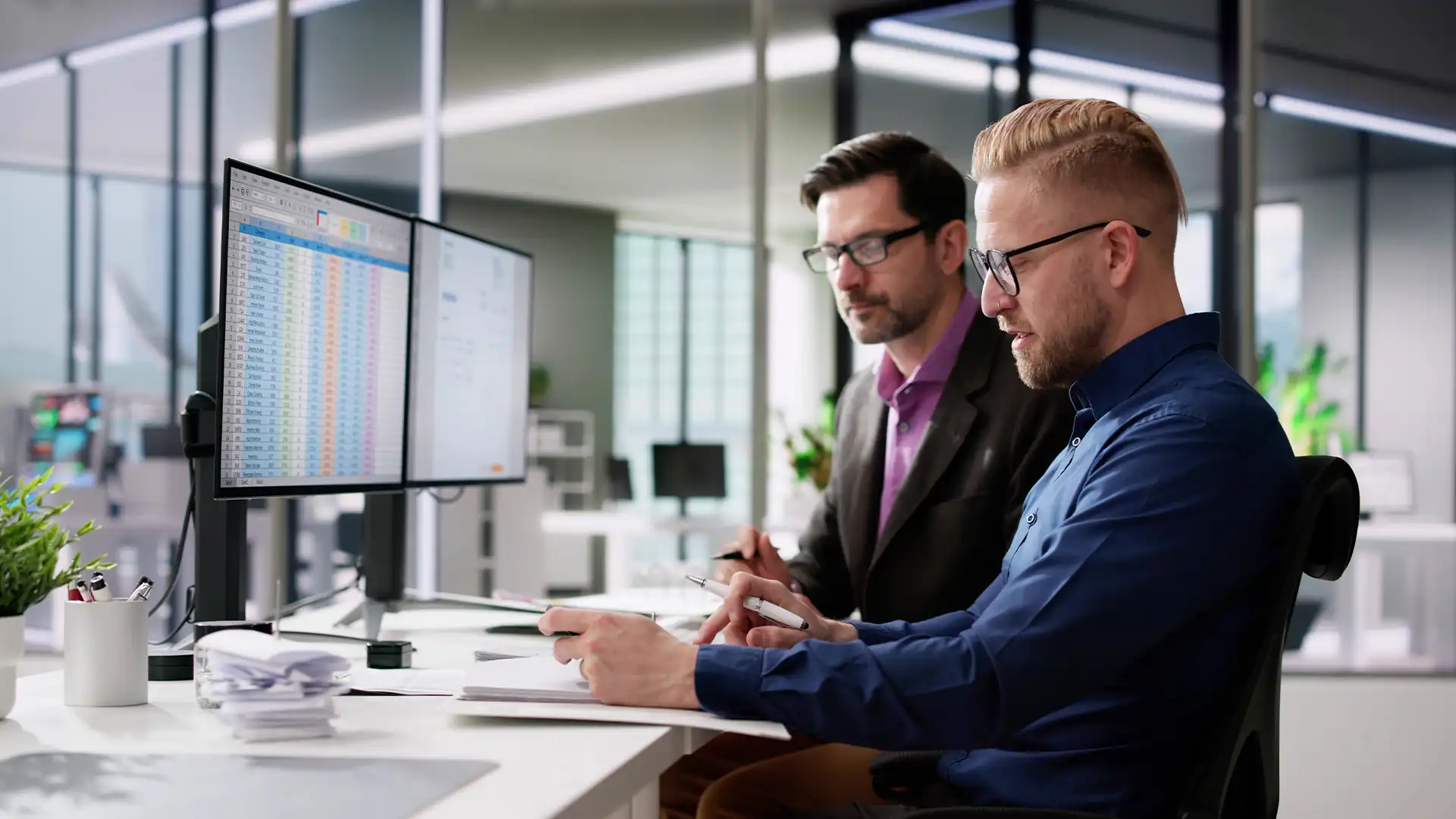 Two corporate experts analyze invoice data on multiple screens, illustrating Prudent's meticulous approach to technology invoice management and cost efficiency