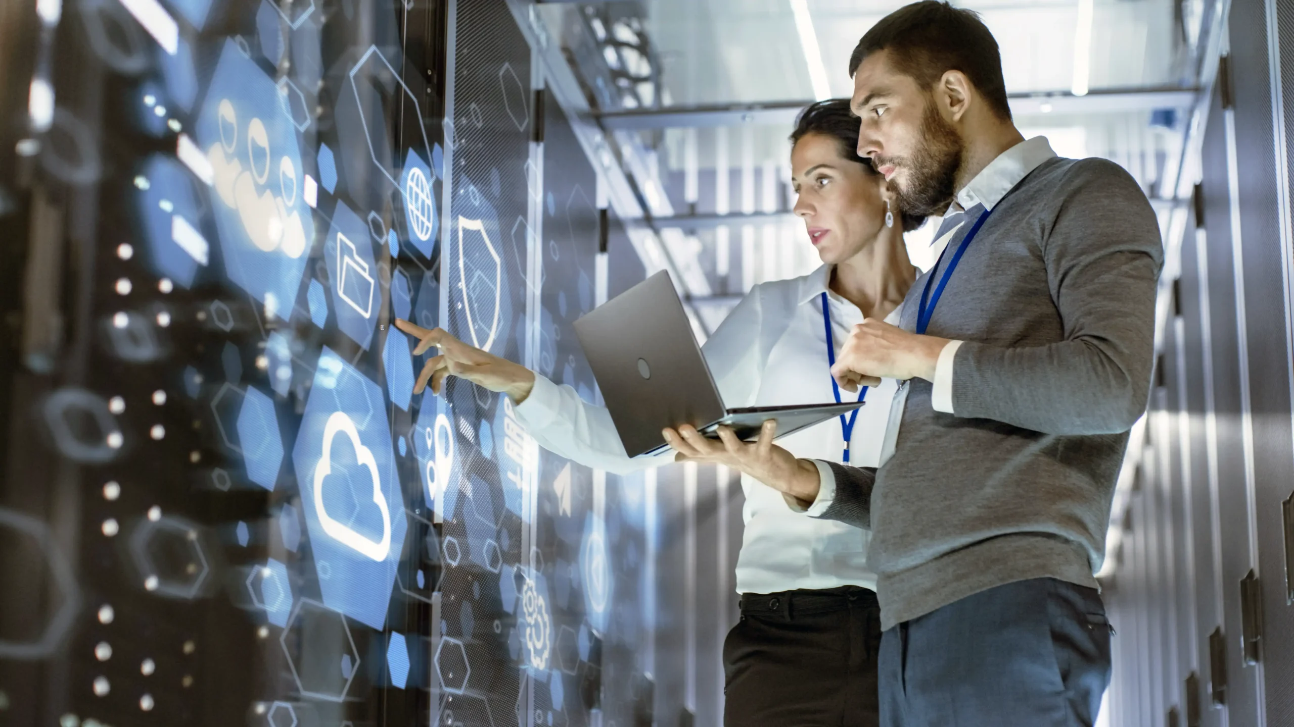 Two IT professionals in a server room using a laptop to analyze and optimize telecom strategies, demonstrating Prudent's commitment to simplifying telecom management to reduce costs and enhance business efficiency